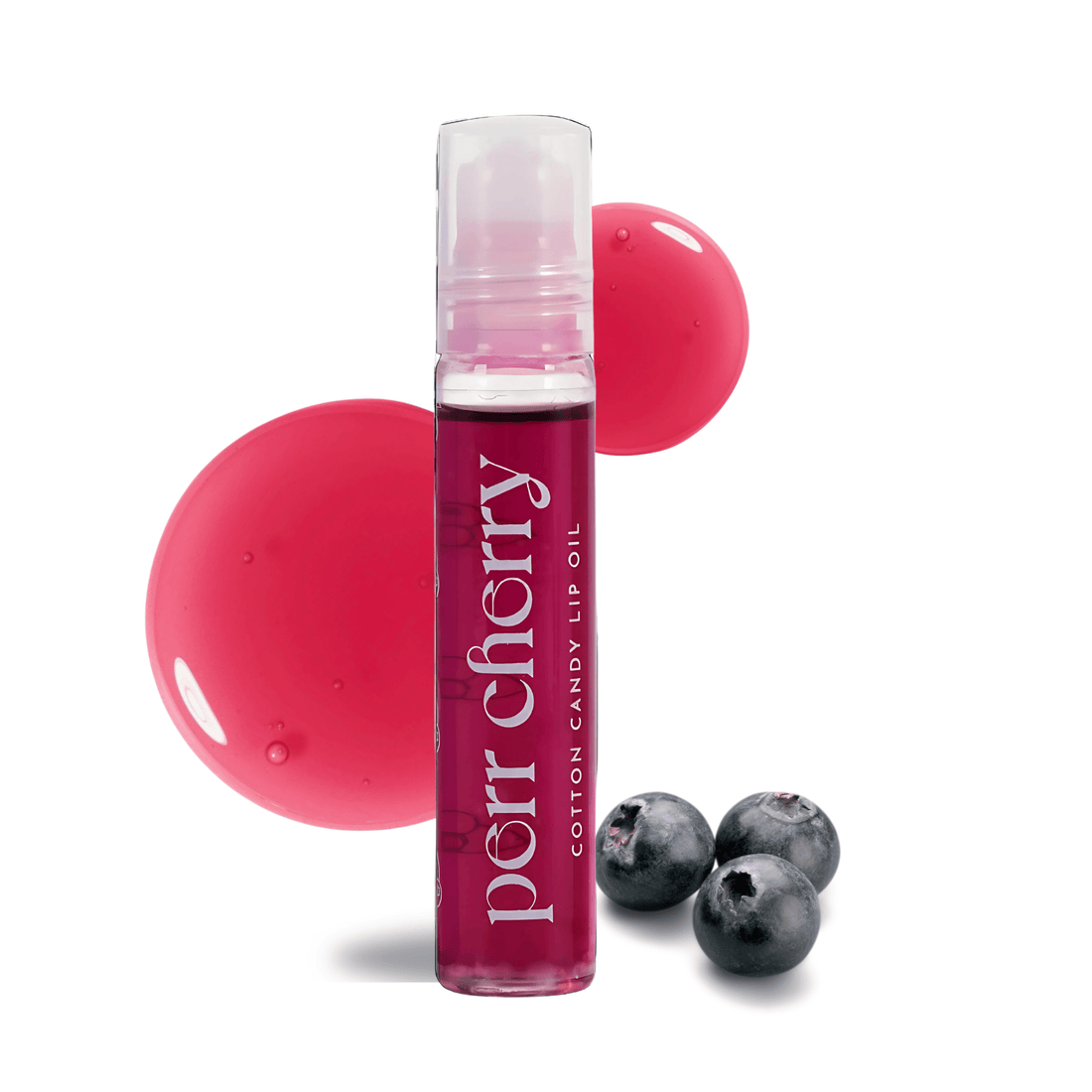 Lip oil bottle with pink cap and visible brand name, surrounded by pink balls and blueberries on a white background.