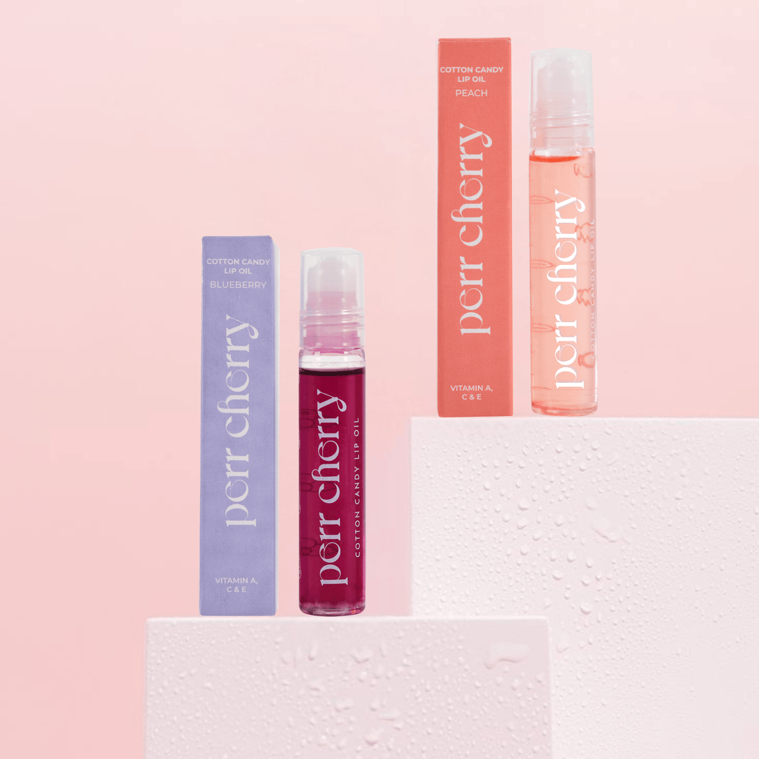 Three Perr Cherry lip gloss products on a pink background